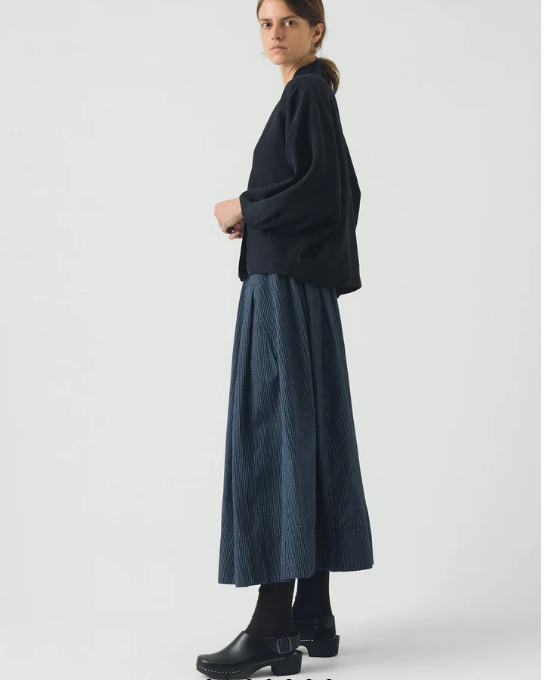 Woman in a dark outfit standing against a white background with a computer interface overlay.