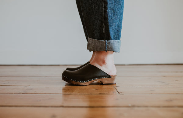 close up of woman's feet in denim jumpsuit with black low classic style swedish clog