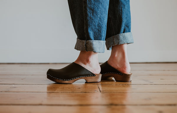 close up of woman's feet in denim jumpsuit with black low classic style swedish clog