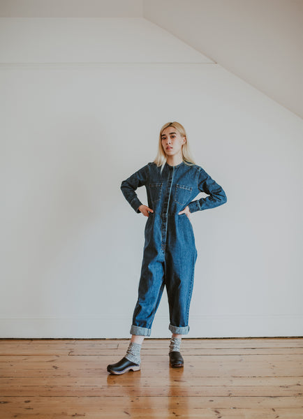 woman wears denim jumpsuit with thick socks and black low classic style swedish clog