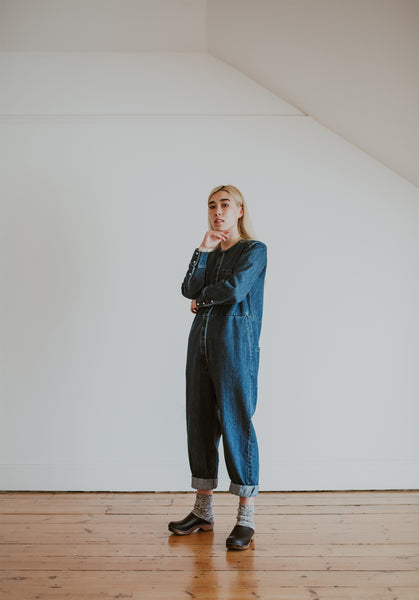 woman wears denim jumpsuit with thick socks and black low classic style swedish clog