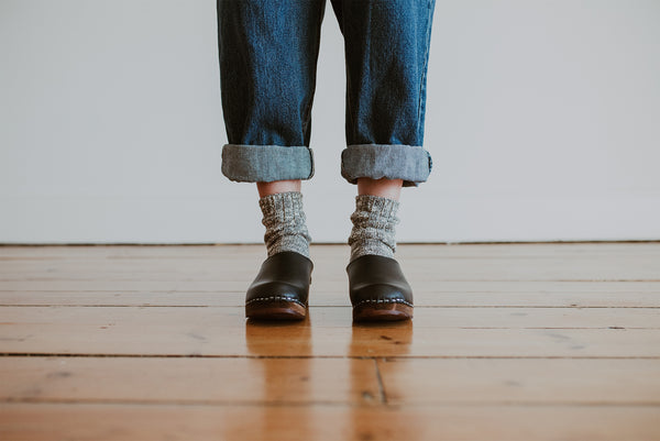 close up of woman's feet in denim jumpsuit with thick socks and black low classic style swedish clog