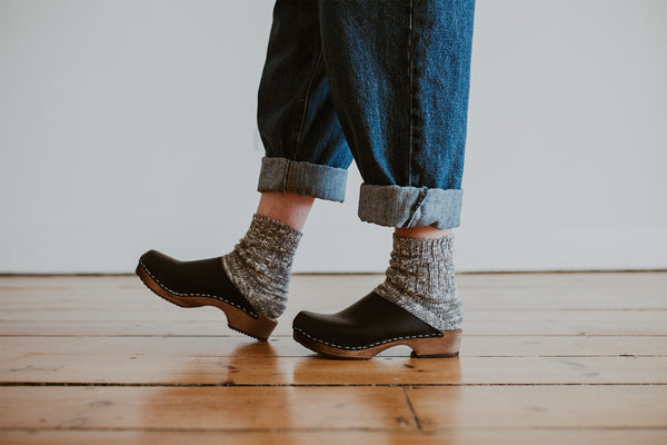 close up of woman's feet in denim jumpsuit with thick socks and black low classic style swedish clog