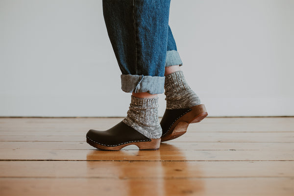 close up of woman's feet in denim jumpsuit with thick socks and black low classic style swedish clog