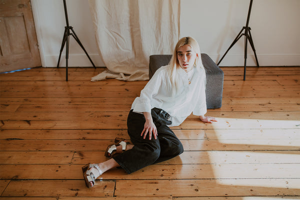 girl poses wearing a white shirt and black wide leg jeans with silver cross over mid heel clog sandals