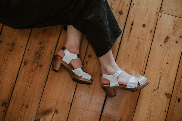 girl poses wearing a white shirt and black wide leg jeans with silver cross over mid heel clog sandals