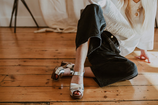 girl poses wearing a white shirt and black wide leg jeans with silver cross over mid heel clog sandals