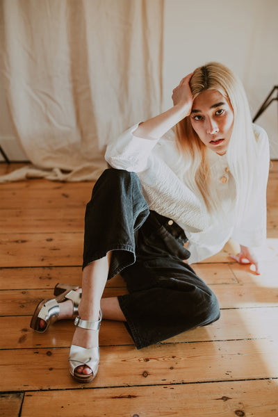 girl poses wearing a white shirt and black wide leg jeans with silver cross over mid heel clog sandals