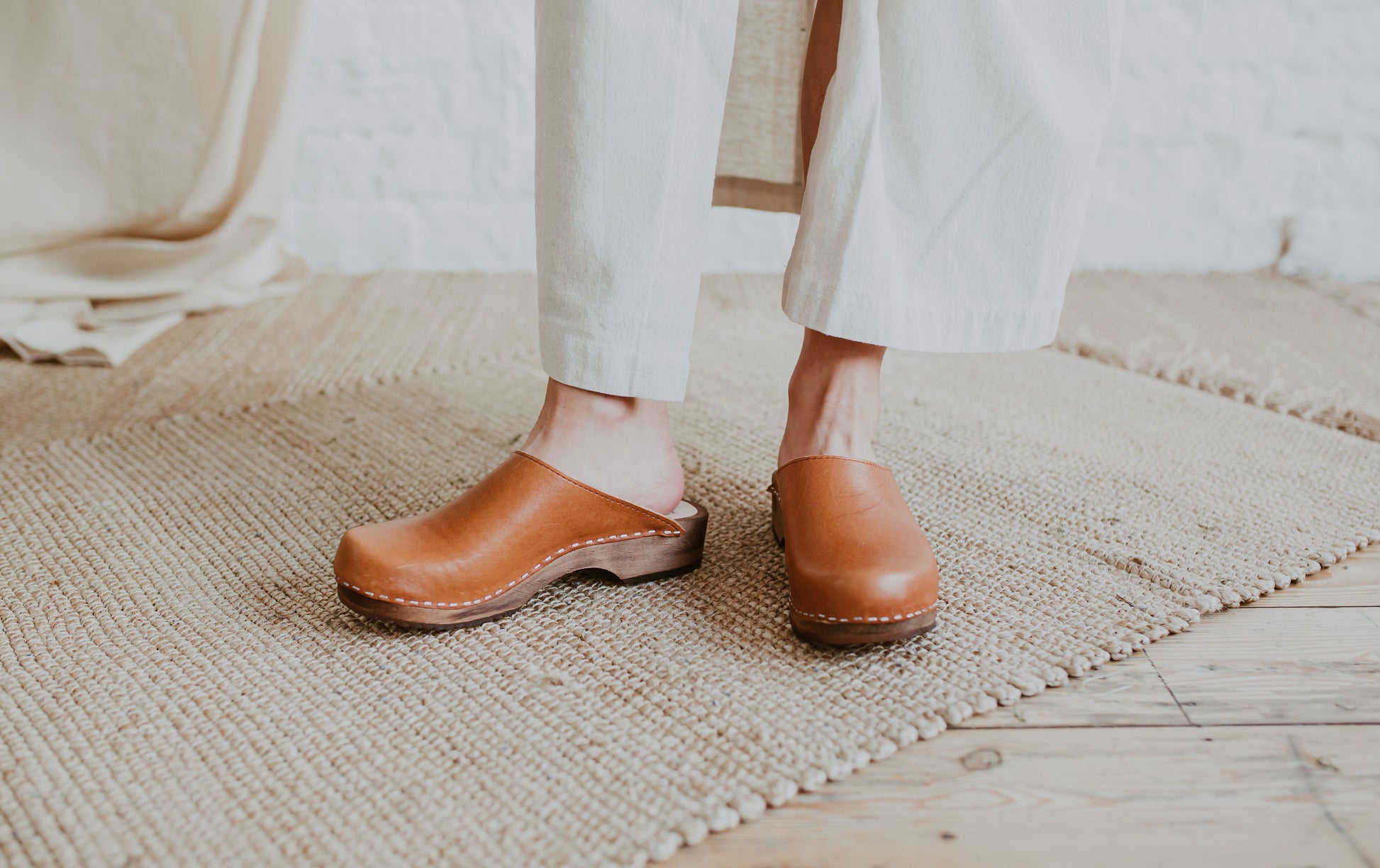 close up of woman's feet wearing a raw beige coloured linen skirt and cumin orangey tan brown low classic style swedish clogs